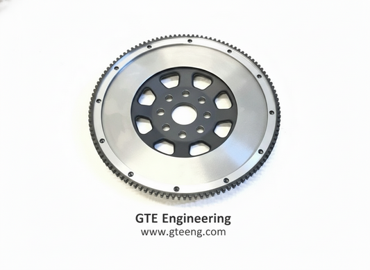Original flywheel service-example image showing a silver friction face, black center and toothed ring gear; exact application varies.