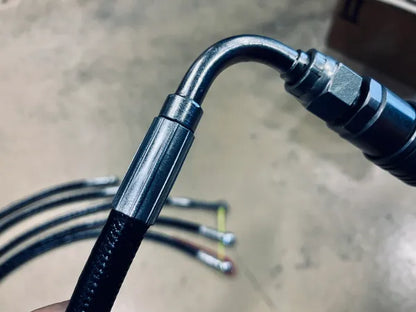 Original shared hydraulic-hose workmanship example showing a curved elbow, hex fitting and crimp sleeve on black hose, with blurred hoses behind