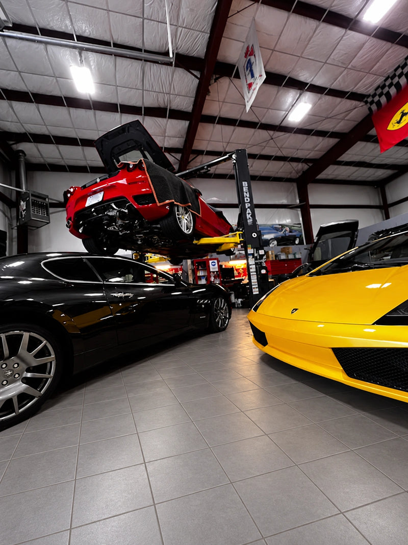 Ferrari on a service lift beside Maserati and Lamborghini vehicles in the GTE Engineering workshop